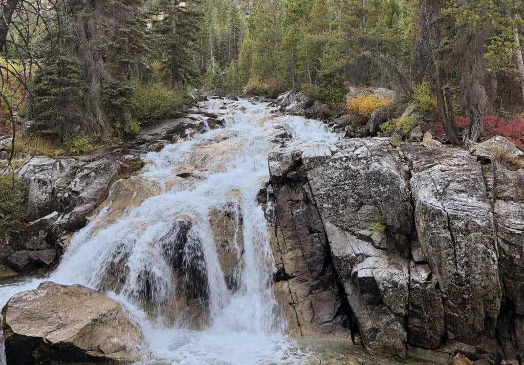 A cascading waterfall flows over rocky terrain surrounded by lush greenery.
