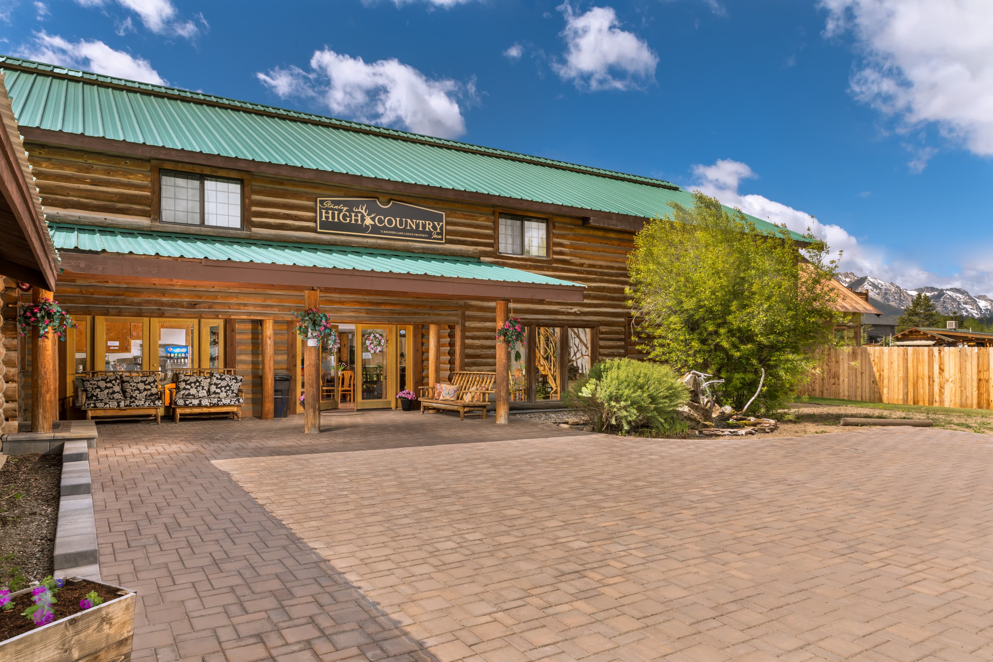 A rustic lodge with a green metal roof and wooden facade, surrounded by trees and a paved entrance.