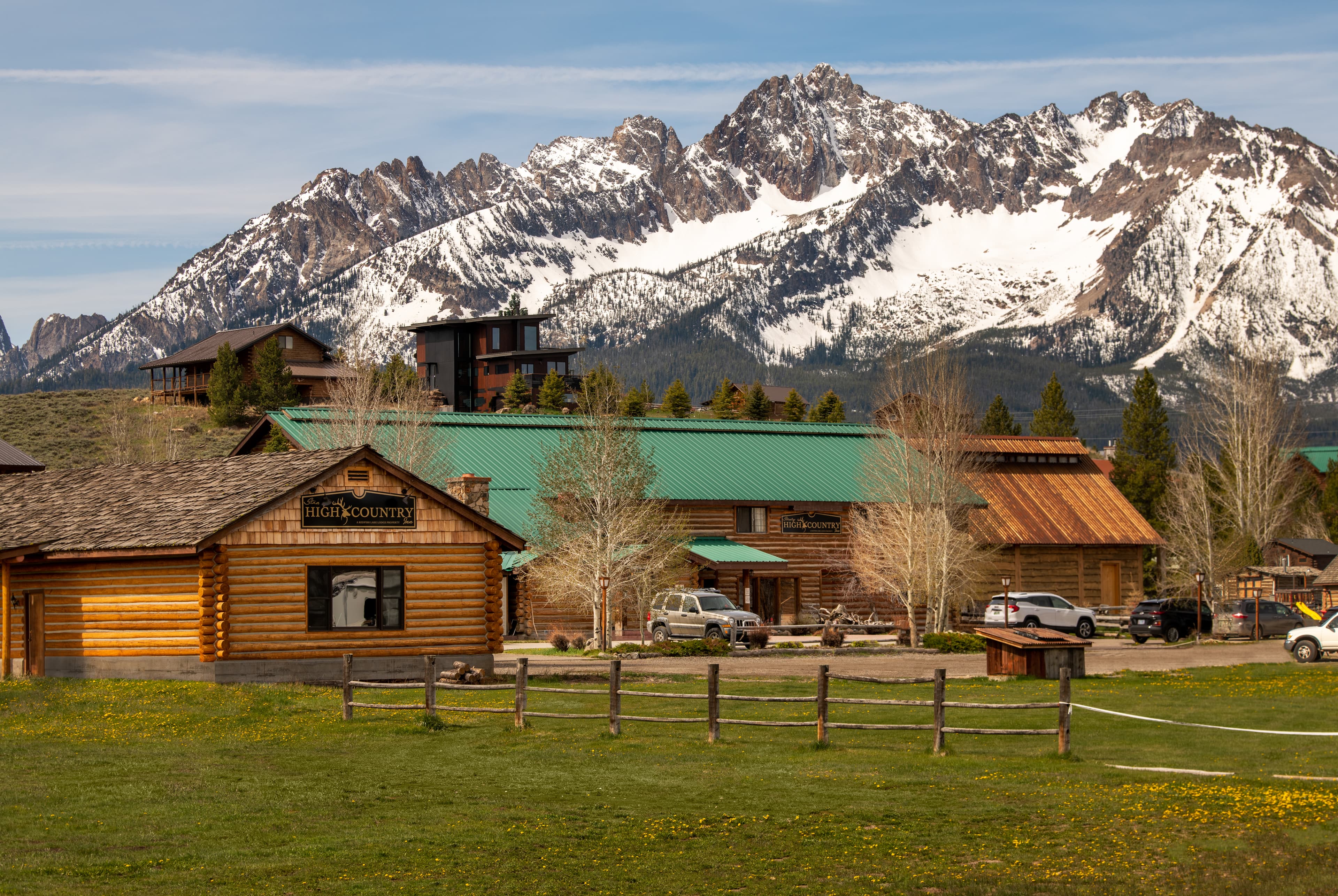 A scenic view of a rustic lodge surrounded by lush green fields and snow-capped mountains in the background.