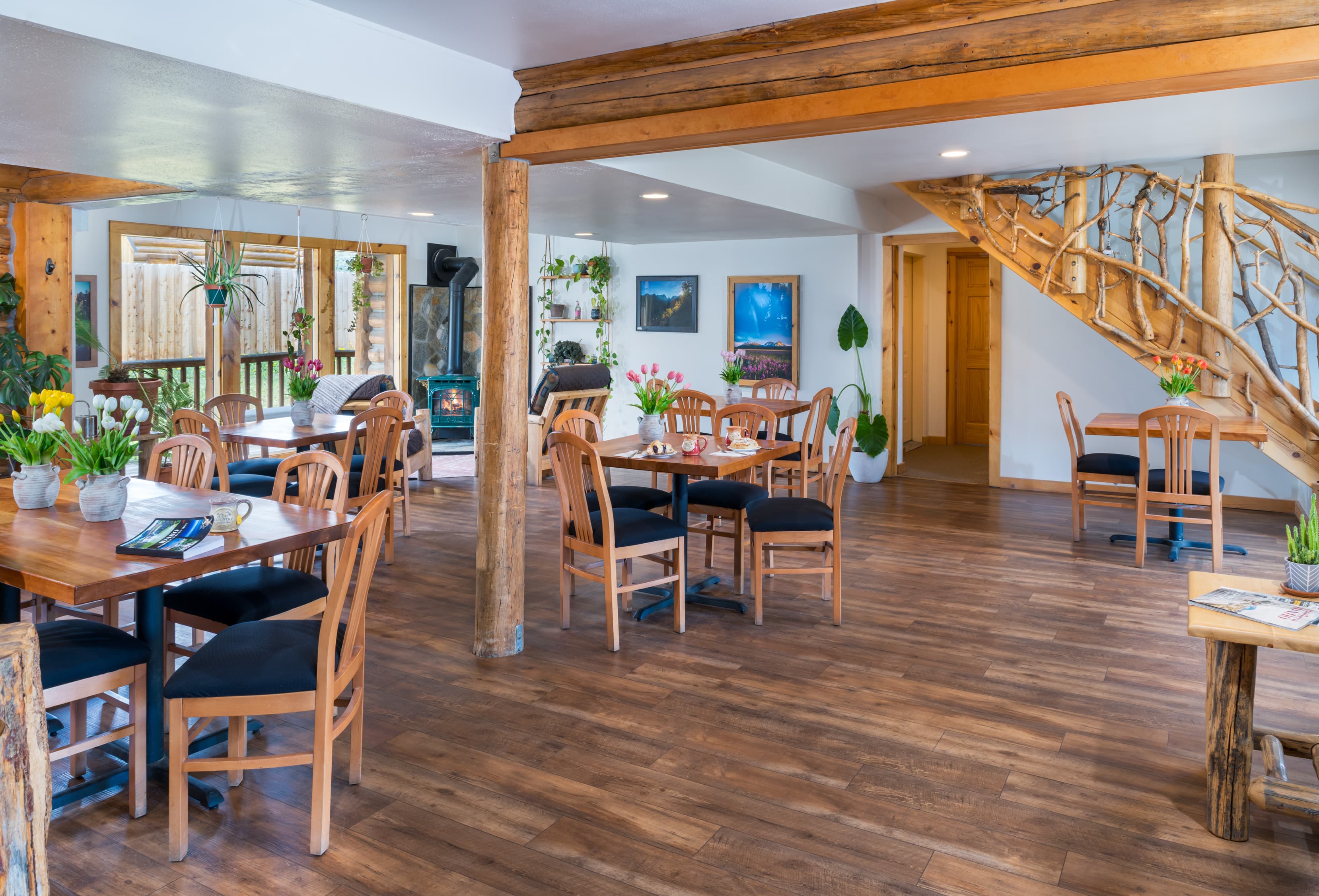 Cozy dining area with wooden tables, chairs, and decorative plants, featuring a staircase in the background.