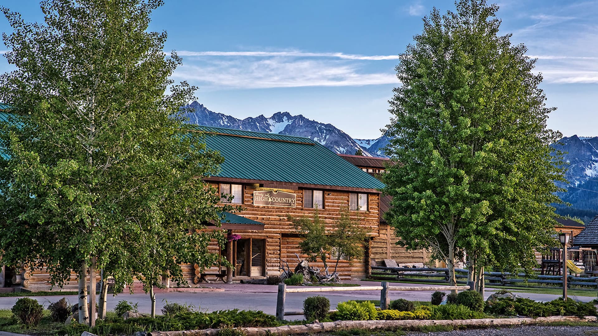 Log cabin-style building surrounded by green trees with mountains in the background.