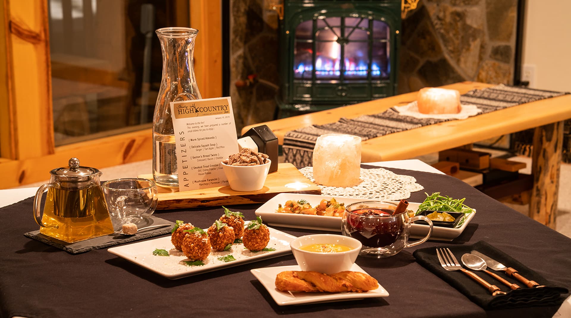 A beautifully arranged dining table with gourmet dishes by a glowing fireplace.
