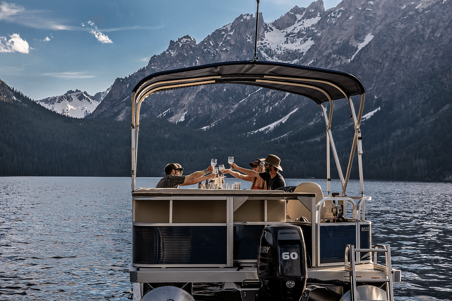 Two people toast with glasses on a boat surrounded by mountains and water.