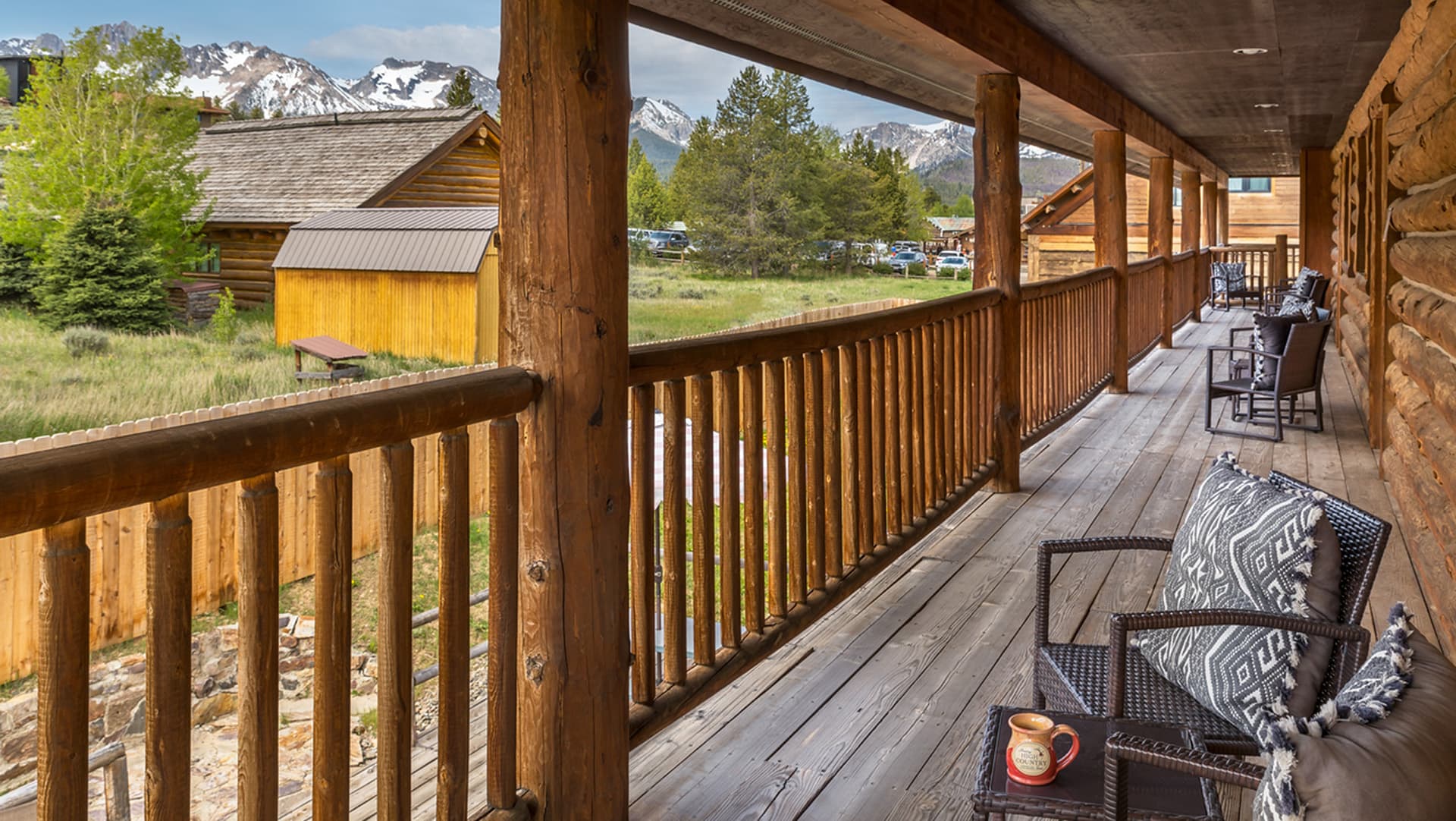 A wooden balcony with chairs overlooks a grassy area and mountains in the background.