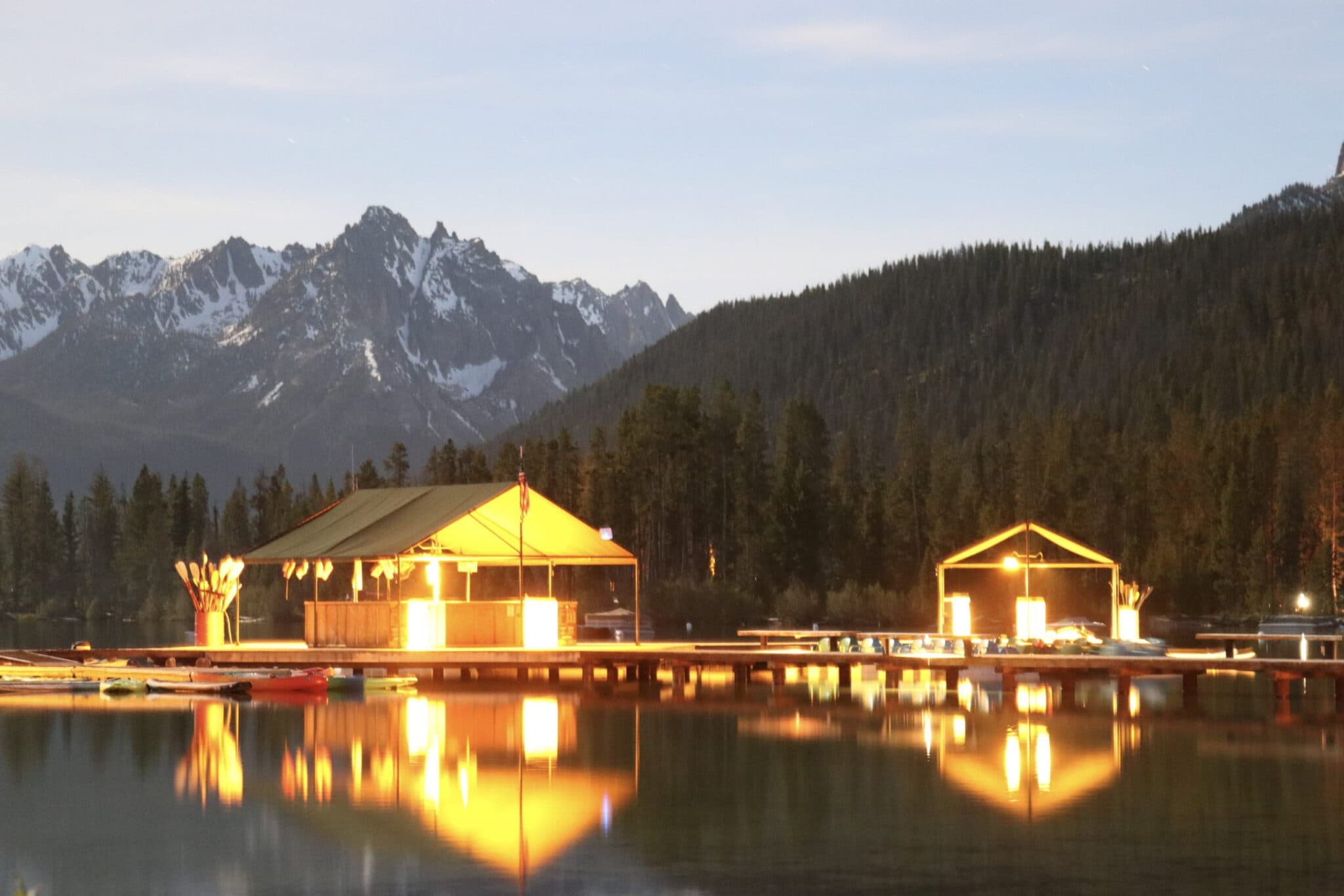 A peaceful lakeside scene under moonlight, featuring illuminated cabins and mountain reflections.
