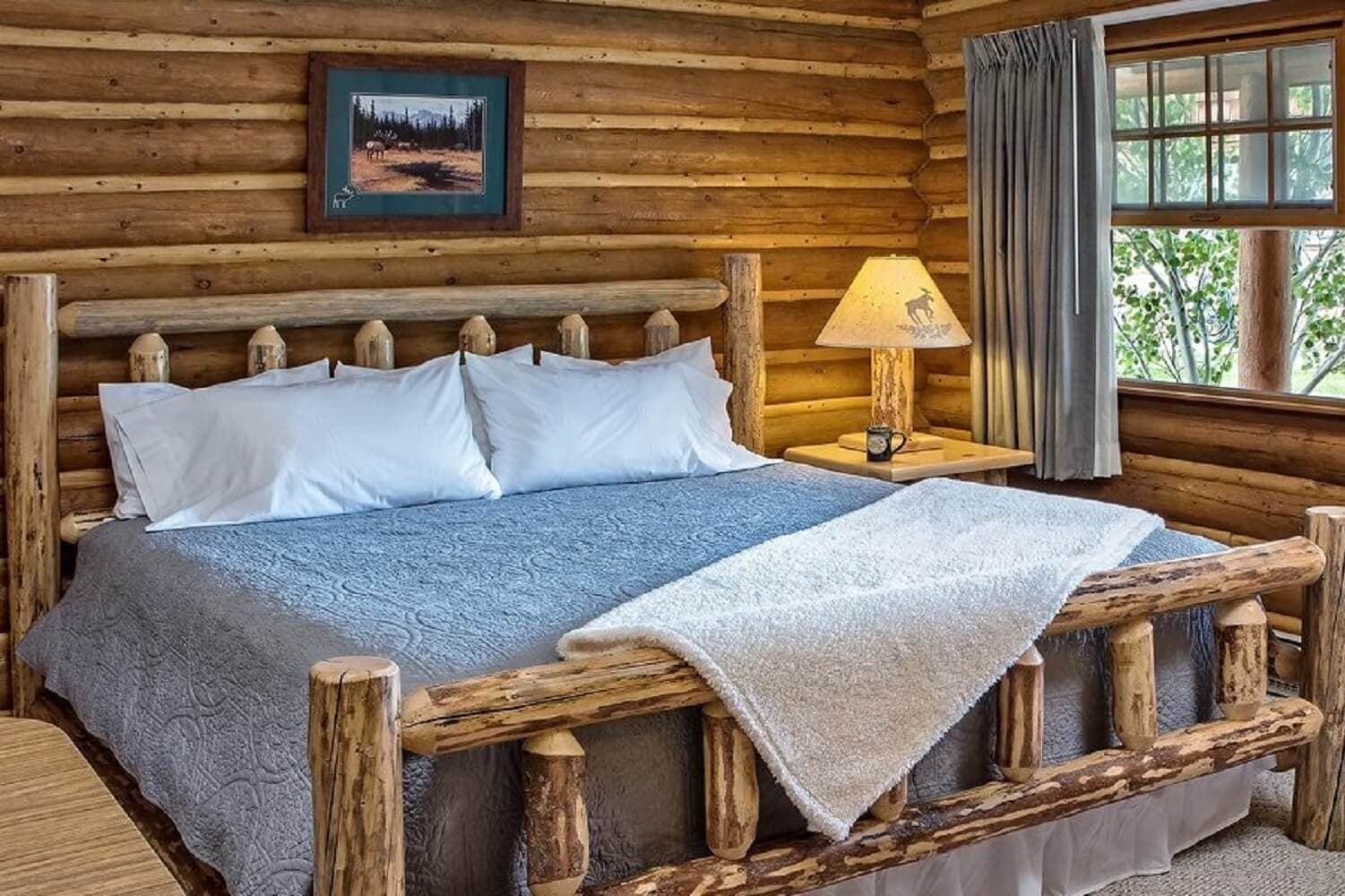 A cozy log cabin bedroom featuring a wooden bed, plush bedding, and a window with natural light.