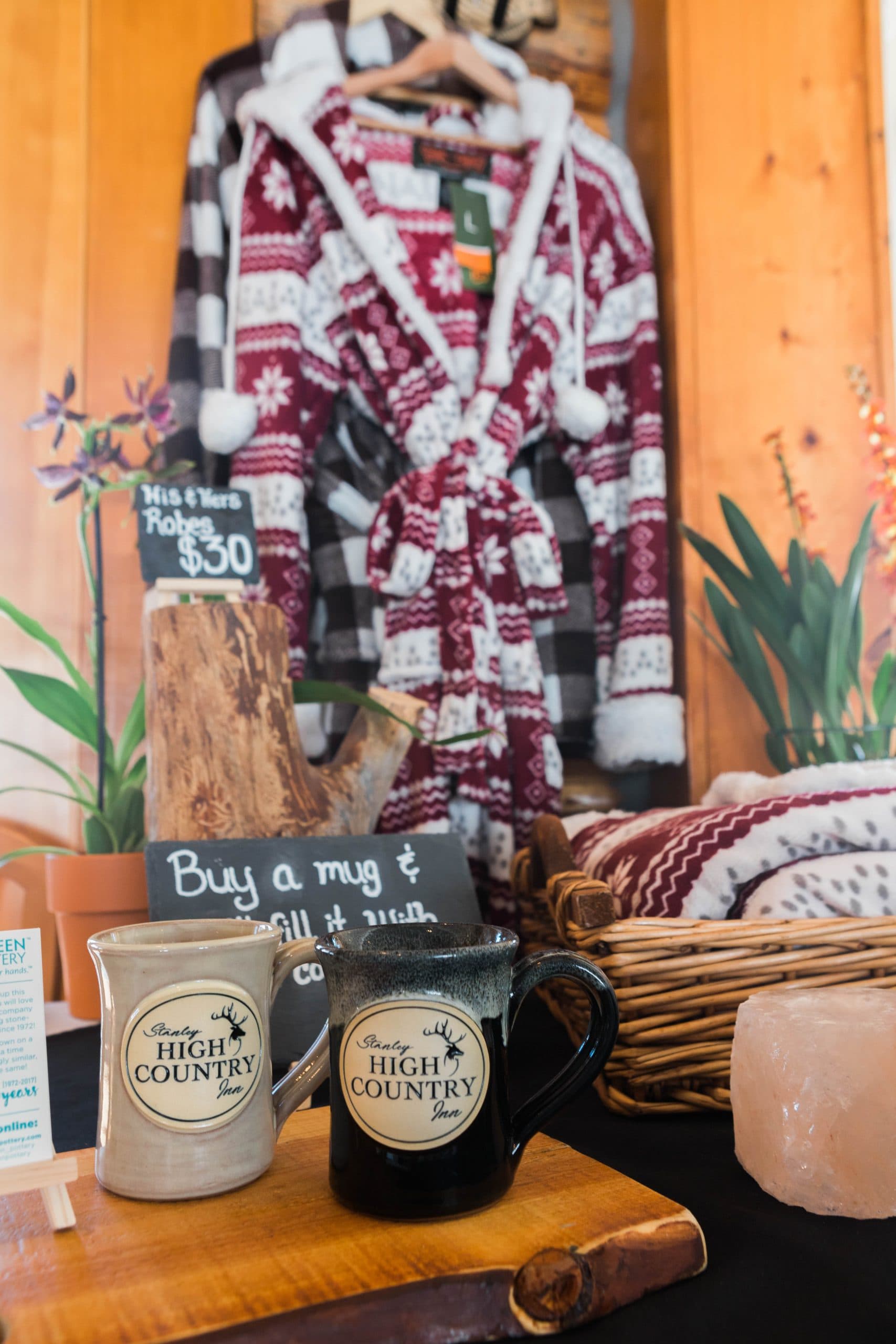A display featuring cozy robes for sale alongside mugs from High Country Inn and decorative items.