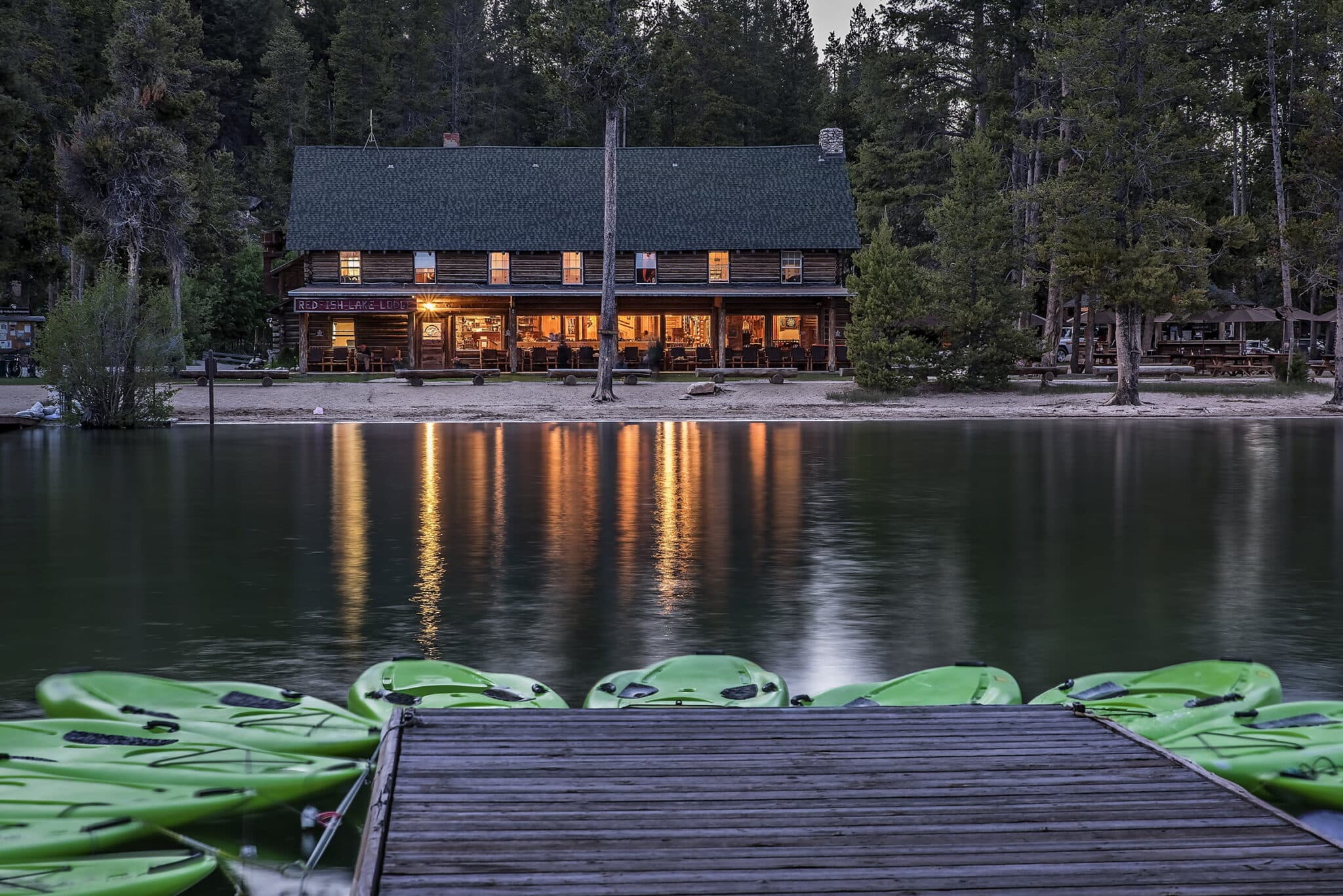 A rustic lodge by a calm lake, with green kayaks lined along a wooden dock at dusk. A rustic lodge by a calm lake, with green kayaks lined along a wooden dock at dusk.