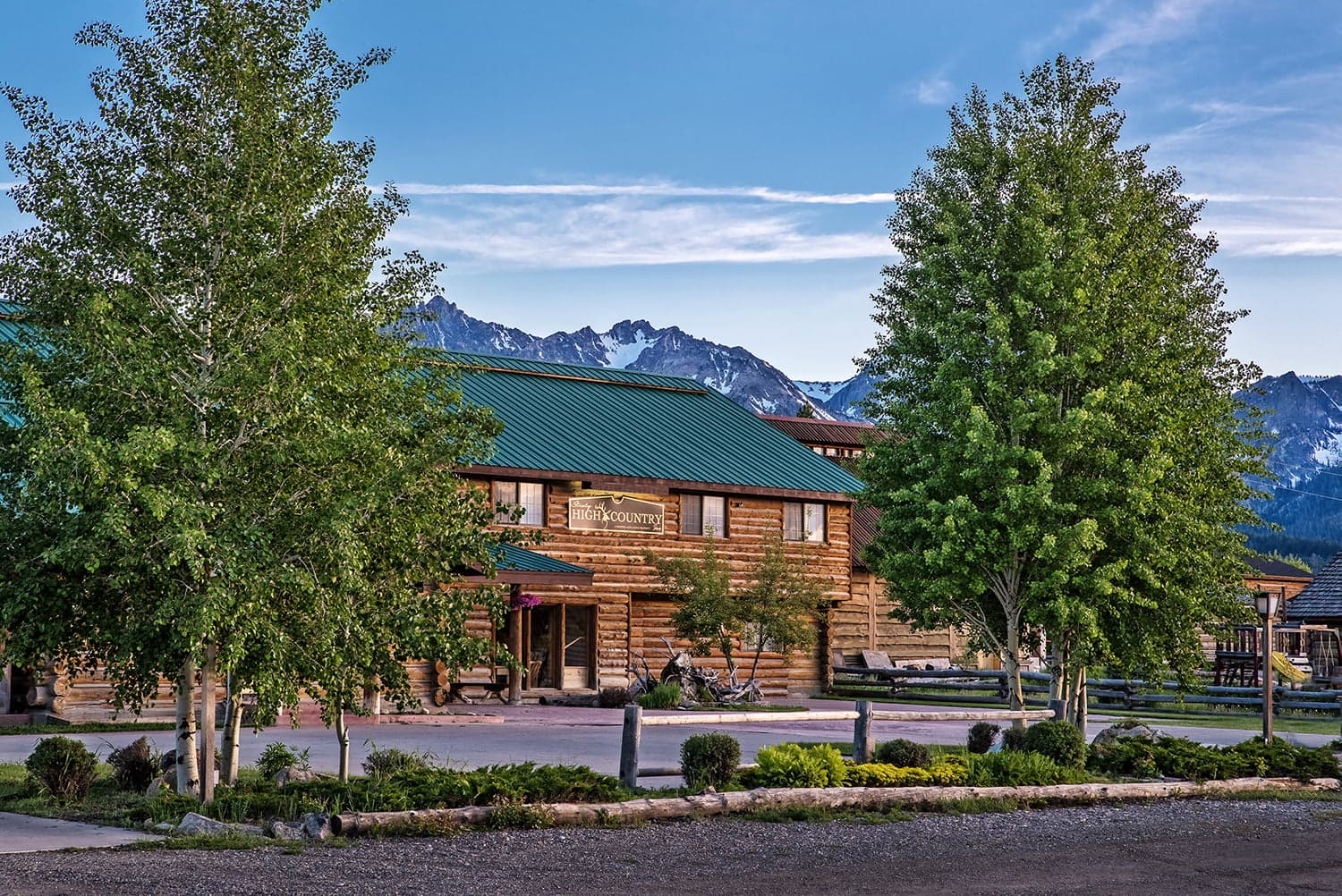 A rustic log cabin-style building surrounded by green trees and mountains in the background.