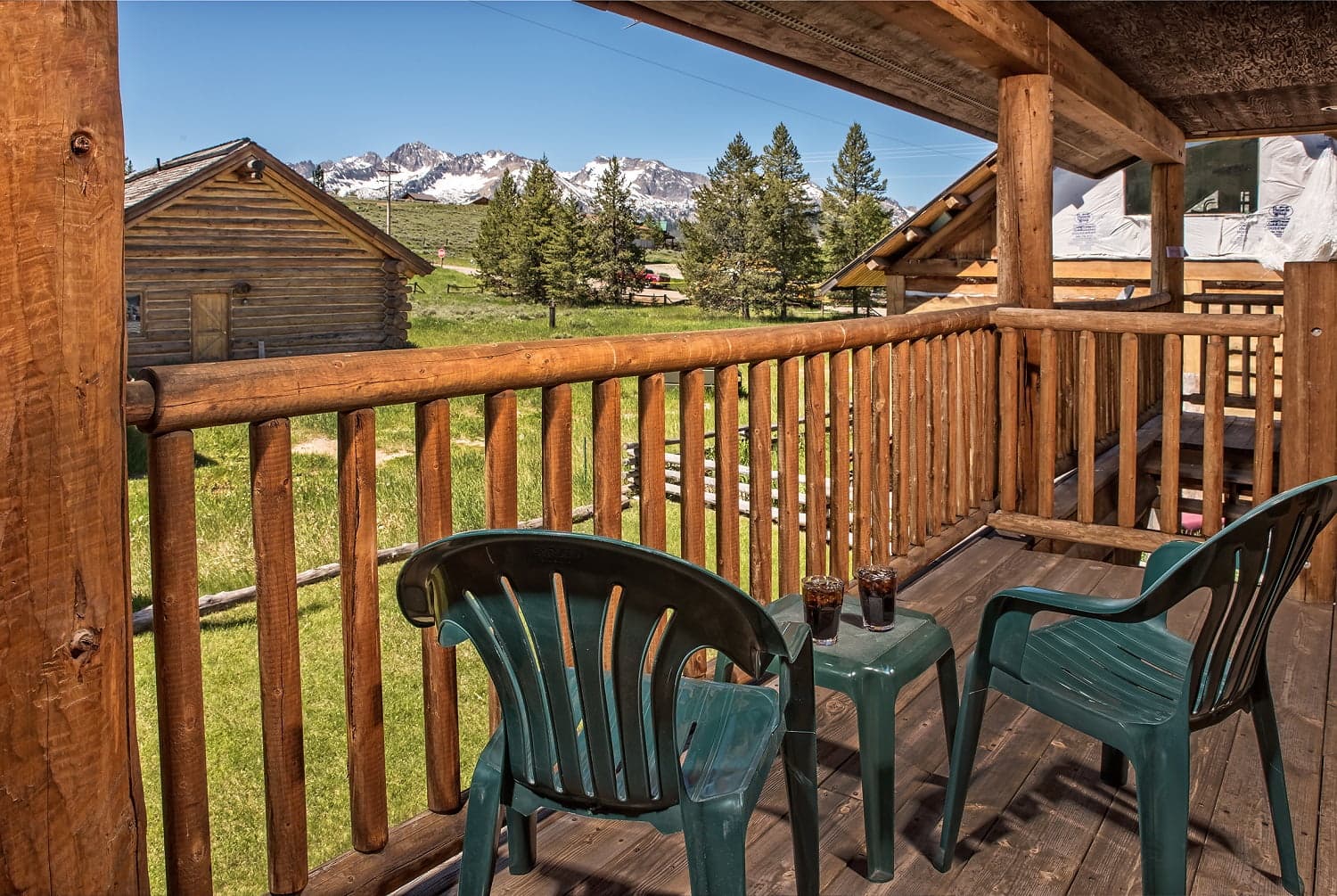 A balcony with two green chairs and drinks overlooks a scenic mountain view.
