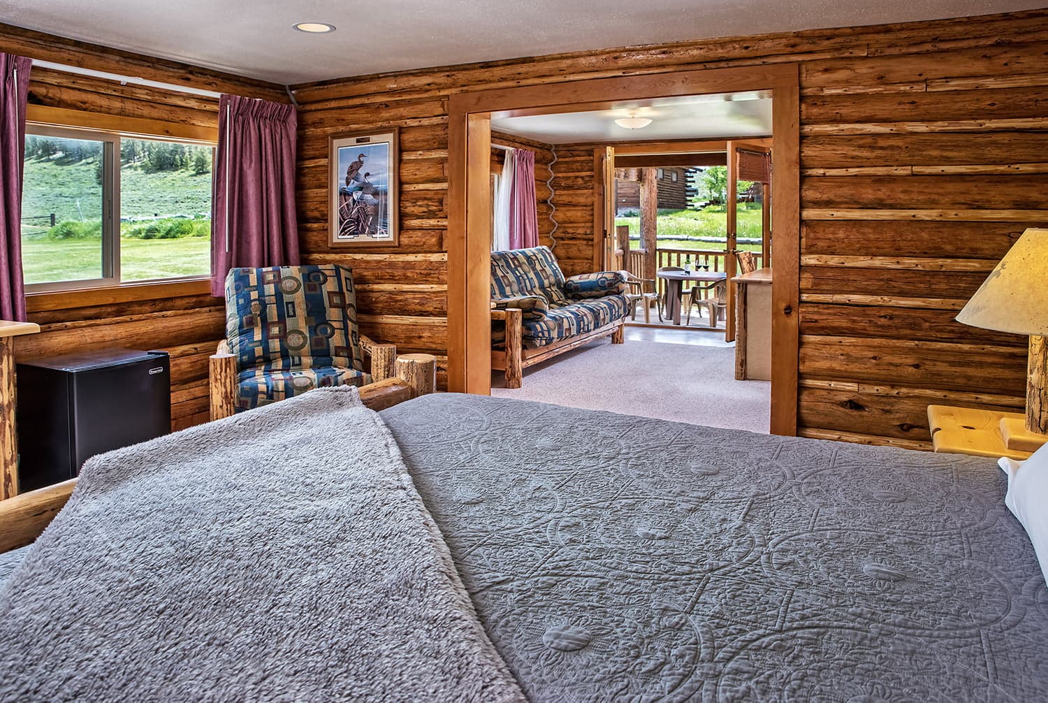 Cozy log cabin room featuring a bed, comfortable seating, and an open view to the outdoors.