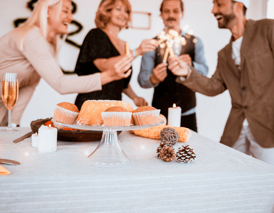 A group of four people celebrate together with sparklers, surrounded by festive treats on a table.