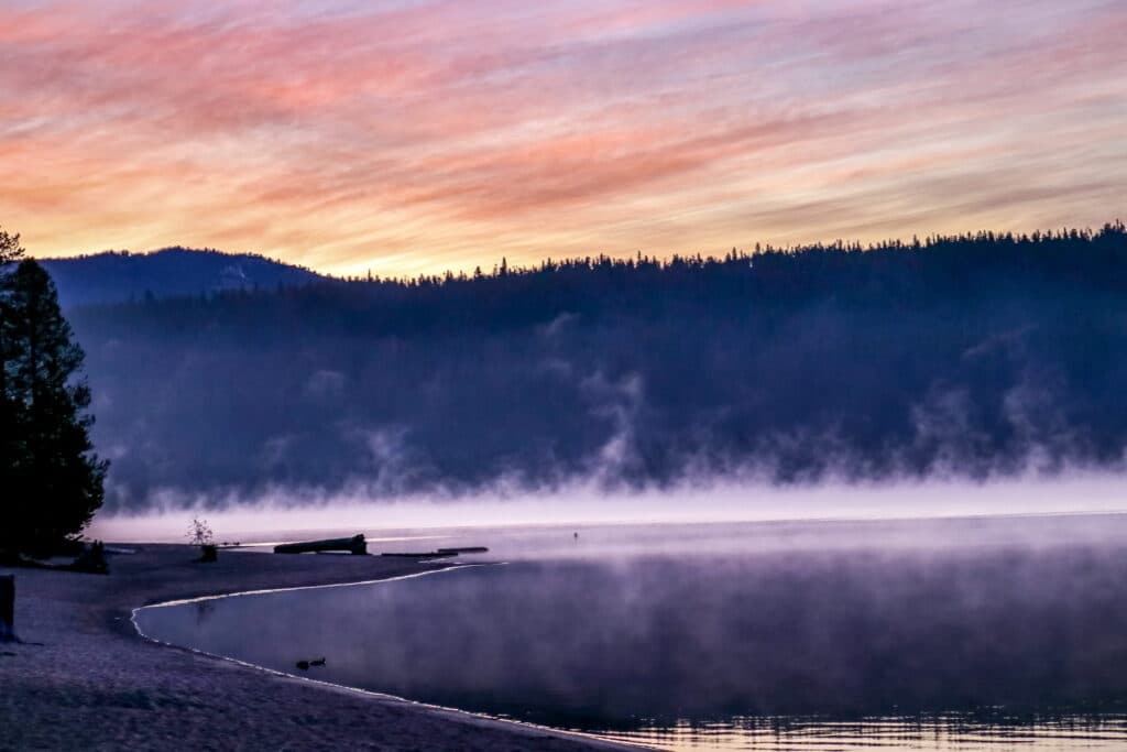 A serene lake at sunrise, surrounded by mist and mountains.