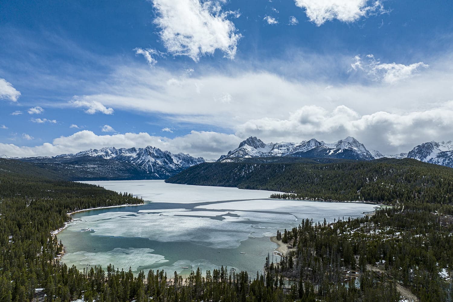 semi frozen alpine lake with snow capped mountains in distance